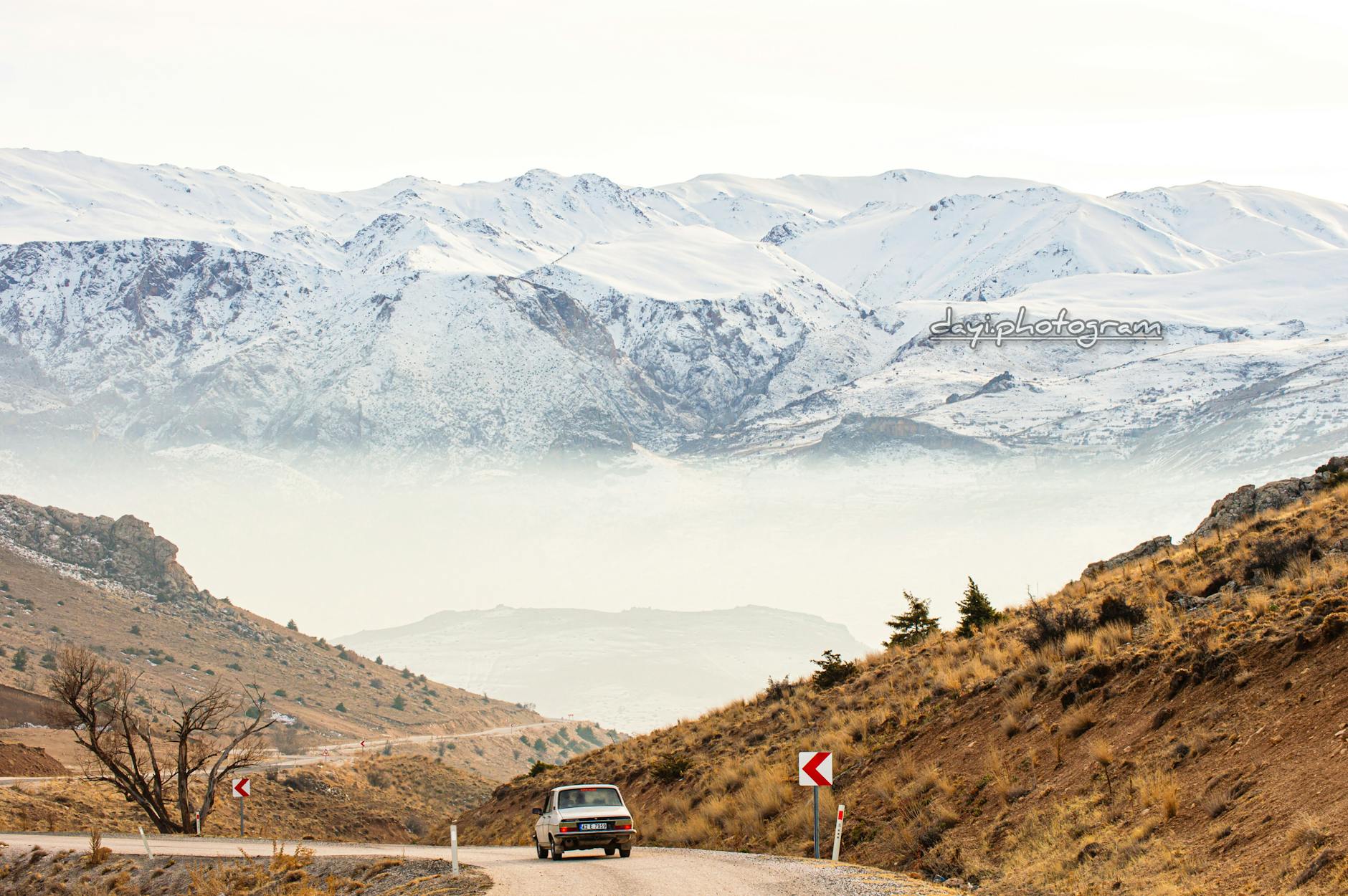 Zabytkowy samochód na górskiej drodze z ośnieżonymi szczytami w tle