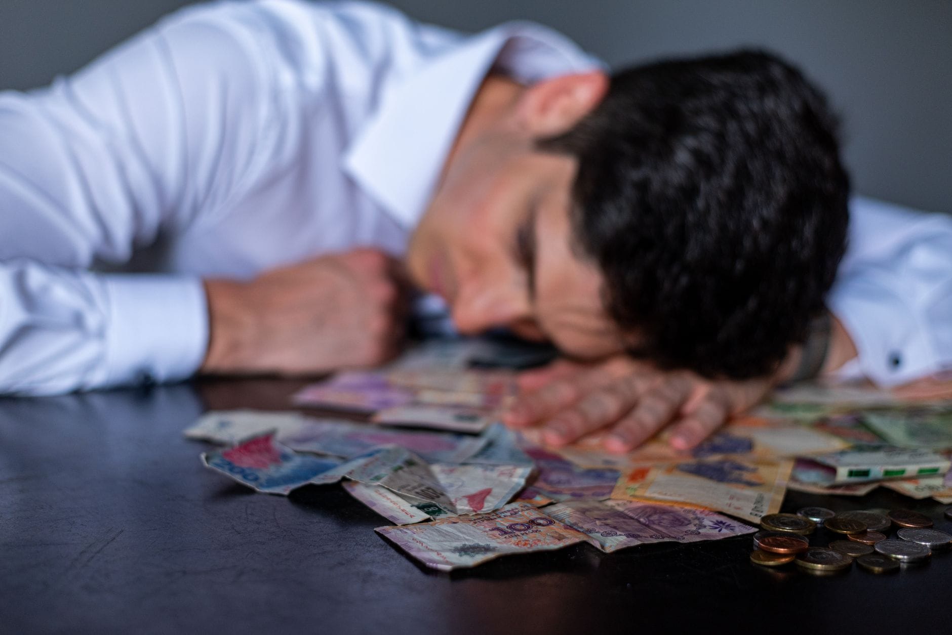 Mężczyzna załamany nad stołem zasłanym banknotami i monetami